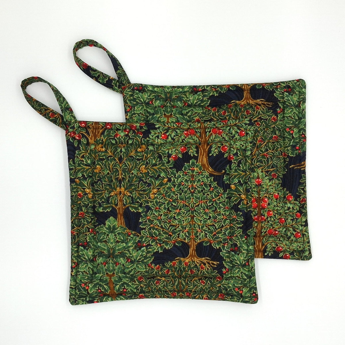 Two square fabric potholders with loop handles, featuring a detailed  tree pattern with red fruit and brown trunks on a dark background.